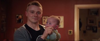 Movie still from “Fighting with My Family” (2019), directed by Stephen Merchant – A man holding a baby in a sling; Close Up shot, Over the shoulder angle