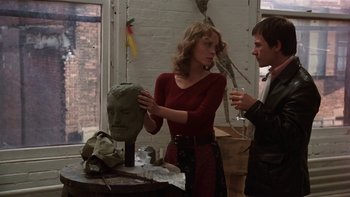 Movie still from “Fingers” (1978), directed by James Toback – A woman standing next to a man next to a sculpture; Close Up shot, Over the shoulder angle