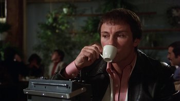 Movie still from “Fingers” (1978), directed by James Toback – A man sitting at a table drinking a cup of coffee; Close Up shot, Low angle