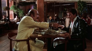 Movie still from “Fingers” (1978), directed by James Toback – Two people sitting at a table in front of plates of food; Medium shot, Low angle