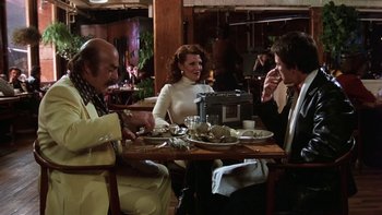 Movie still from “Fingers” (1978), directed by James Toback – A group of people sitting at a table with plates of food; Medium shot, Low angle