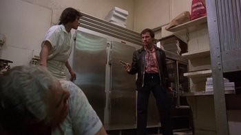 Movie still from “Fingers” (1978), directed by James Toback – A man standing in a kitchen holding a cell phone; Medium shot, Low angle