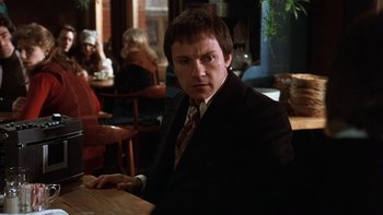 Movie still from “Fingers” (1978), directed by James Toback – A man sitting at a table in front of other people; Medium shot, Low angle