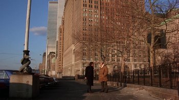Movie still from “Fingers” (1978), directed by James Toback – Two people standing on the side of the road in front of a building; Extreme Wide shot, Over the shoulder angle