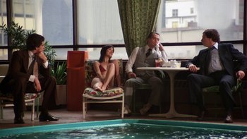 Movie still from “Fingers” (1978), directed by James Toback – A man and a woman sitting at a table near a swimming pool; Wide shot, High angle