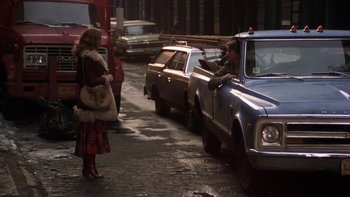 Movie still from “Fingers” (1978), directed by James Toback – A woman is standing next to a car on the side of the road; Wide shot, Over the shoulder angle