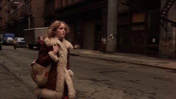 Movie still from “Fingers” (1978), directed by James Toback – A woman walking down the street wearing a brown coat; Wide shot, Low angle