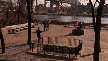 Movie still from “Fingers” (1978), directed by James Toback – A group of people standing on a sidewalk next to a river; Extreme Wide shot, High angle