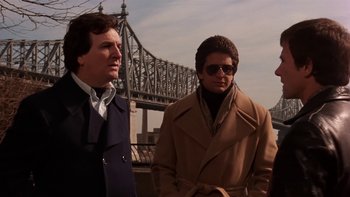 Movie still from “Fingers” (1978), directed by James Toback – Two men standing next to each other near a bridge; Medium shot, Low angle