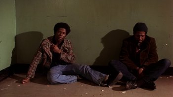 Movie still from “Fingers” (1978), directed by James Toback – Two men sitting on the ground in front of a green wall; Medium shot, High angle