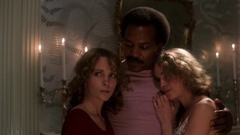 Movie still from “Fingers” (1978), directed by James Toback – A man and two women standing next to each other in front of candles; Medium shot, Low angle