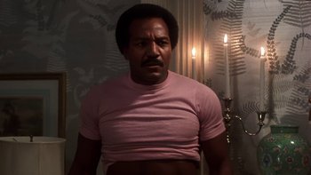 Movie still from “Fingers” (1978), directed by James Toback – A man in a t - shirt standing in front of candles; Medium shot, Low angle