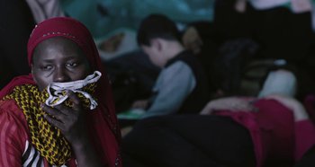 A woman wearing a red headscarf is holding a cell phone in her hand