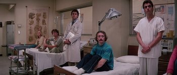 Movie still from “Firestarter” (1984), directed by Mark L. Lester – A man sitting on a hospital bed while a doctor watches; Wide shot, Low angle