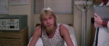 Movie still from “Firestarter” (1984), directed by Mark L. Lester – A man sitting on top of a bed in a room; Close Up shot, Low angle