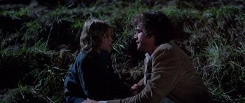 Movie still from “Firestarter” (1984), directed by Mark L. Lester – A man sitting next to a young girl in the grass; Medium shot, Over the shoulder angle