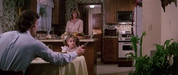 Movie still from “Firestarter” (1984), directed by Mark L. Lester – A young girl sitting at a table in a kitchen with an older woman; Medium shot, Over the shoulder angle