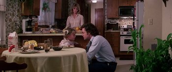 Movie still from “Firestarter” (1984), directed by Mark L. Lester – A man and a woman sitting at a table with a cake on it; Medium shot, Over the shoulder angle