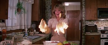 Movie still from “Firestarter” (1984), directed by Mark L. Lester – A woman in a kitchen holding fire in her hands; Medium shot, Low angle