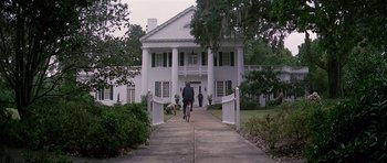 Movie still from “Firestarter” (1984), directed by Mark L. Lester – A man riding a bike down a sidewalk near a house; Extreme Wide shot, Low angle