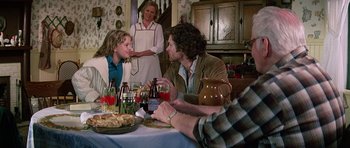 Movie still from “Firestarter” (1984), directed by Mark L. Lester – A group of people sitting around a table with food; Medium shot, Over the shoulder angle