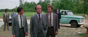 Movie still from “Firestarter” (1984), directed by Mark L. Lester – Two men in suits standing next to each other in a field; Medium shot, Over the shoulder angle