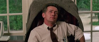 Movie still from “Firestarter” (1984), directed by Mark L. Lester – A man sitting in an office chair wearing a tie; Close Up shot, Low angle