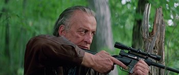 Movie still from “Firestarter” (1984), directed by Mark L. Lester – An older man is holding a rifle and aiming it; Close Up shot, Low angle