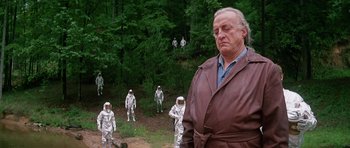 Movie still from “Firestarter” (1984), directed by Mark L. Lester – An old man in a brown robe standing in front of a group of astronauts; Medium shot, Over the shoulder angle
