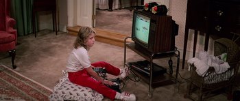 Movie still from “Firestarter” (1984), directed by Mark L. Lester – A little girl sitting in front of a tv playing a video game; Medium shot, High angle