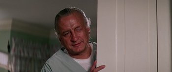 Movie still from “Firestarter” (1984), directed by Mark L. Lester – An older man in a white shirt is standing by a white door; Close Up shot, Low angle