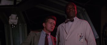 Movie still from “Firestarter” (1984), directed by Mark L. Lester – Two men standing next to each other wearing suits and bow ties; Medium shot, Low angle