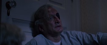 Movie still from “Firestarter” (1984), directed by Mark L. Lester – An older man with a bandaged eye sits in a dark room; Close Up shot, High angle