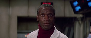 Movie still from “Firestarter” (1984), directed by Mark L. Lester – An older black man wearing a white lab coat; Close Up shot, Low angle