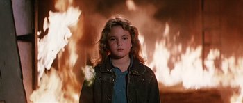 Movie still from “Firestarter” (1984), directed by Mark L. Lester – A young girl standing in front of a burning building; Medium shot, Low angle