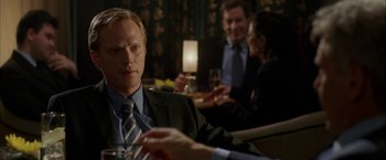 Movie still from “Firewall” (2006), directed by Richard Loncraine – A man sitting at a table with a glass of wine; Close Up shot, Over the shoulder angle