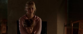 Movie still from “Firewall” (2006), directed by Richard Loncraine – A woman standing next to a boy in a dark room; Medium shot, Over the shoulder angle