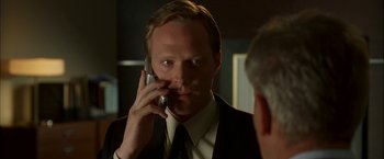 Movie still from “Firewall” (2006), directed by Richard Loncraine – A man in a suit and tie talking on a cell phone in front of a mirror; Close Up shot, Over the shoulder angle
