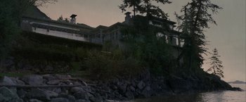 Movie still from “Firewall” (2006), directed by Richard Loncraine – A large house sitting on top of a hill near a body of water; Extreme Wide shot, High angle