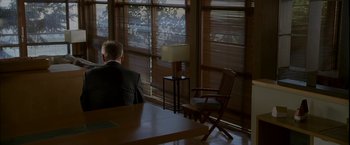 Movie still from “Firewall” (2006), directed by Richard Loncraine – A man sitting at a table in front of a large window; Wide shot, Over the shoulder angle
