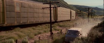 Movie still from “Firewall” (2006), directed by Richard Loncraine – A train traveling down train tracks next to a power pole; Extreme Wide shot, High angle