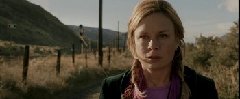 Movie still from “Firewall” (2006), directed by Richard Loncraine – A woman standing on a dirt road near a field; Close Up shot, Low angle