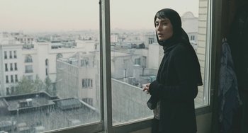 A woman standing in front of a window looking out at a city