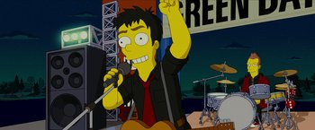 Movie still from “The Simpsons Movie” (2007), directed by David Silverman – A man in a black shirt is holding a microphone; Medium shot, Low angle