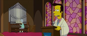 Movie still from “The Simpsons Movie” (2007), directed by David Silverman – A man is standing at a podium in front of a microphone; Medium shot, Low angle