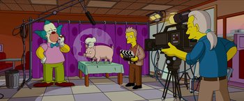 Movie still from “The Simpsons Movie” (2007), directed by David Silverman – A man is standing in front of a pig on a table; Wide shot, Over the shoulder angle