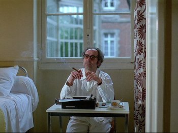 Movie still from “First Name: Carmen” (1983), directed by Jean-Luc Godard – A man sitting at a table with a cigarette in his mouth; Medium shot, Low angle