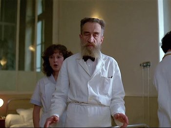 Movie still from “First Name: Carmen” (1983), directed by Jean-Luc Godard – An older man with a long beard standing next to a young woman; Medium shot, Low angle