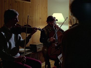 Movie still from “First Name: Carmen” (1983), directed by Jean-Luc Godard – A group of people playing musical instruments in a room; Medium shot, Low angle