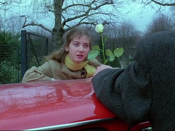 Movie still from “First Name: Carmen” (1983), directed by Jean-Luc Godard – A young woman sitting on the hood of a red car; Close Up shot, Over the shoulder angle